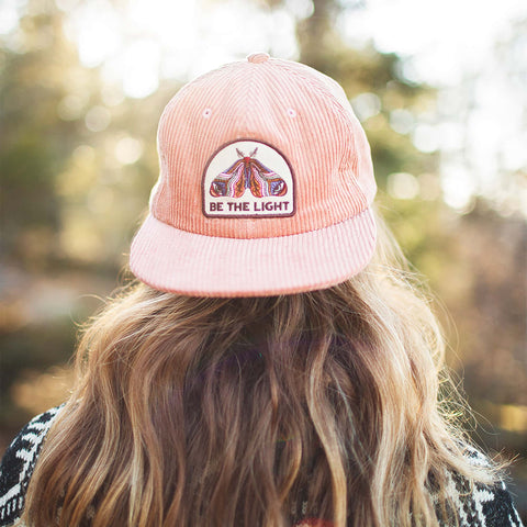 Be The Light hat with painted moth design, 6-panel snapback, flat brim, in a scenic outdoor setting. Trek Light style for all.