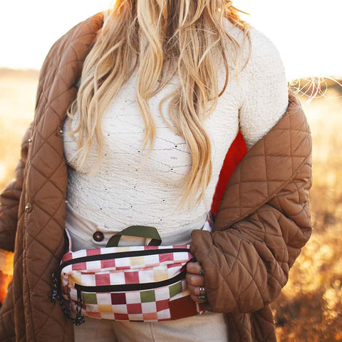 Woman wearing Trek Light Everyday Fanny Pack with checkered design, styled as a hip pack over a white sweater and brown jacket.