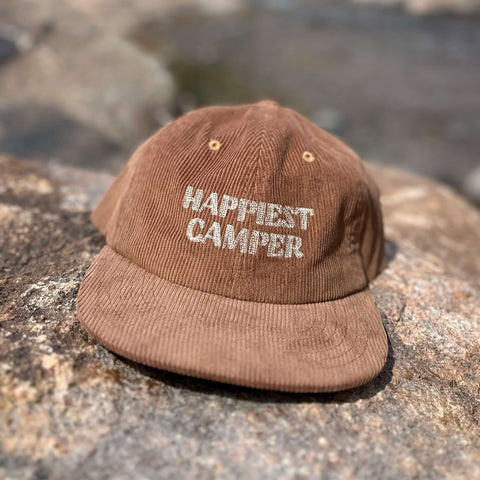 Trek Light Happiest Camper hat on rocks, 6-panel snapback, 100% cotton corduroy for outdoor adventures.