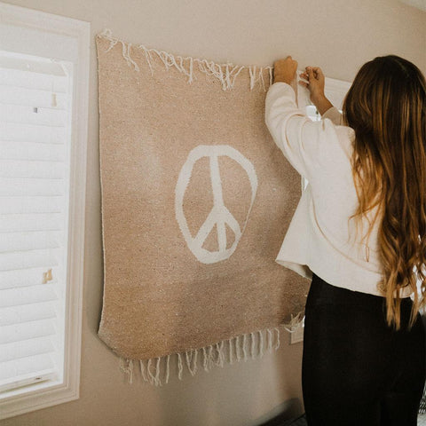 Woman hanging Peace Blanket Art on wall, featuring handwoven design by Trek Light for home decor
