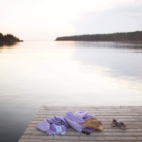 Lavender Sonoma Blanket on a lakeside dock, showcasing its cozy, handwoven design made from recycled clothing materials. By Trek Light.