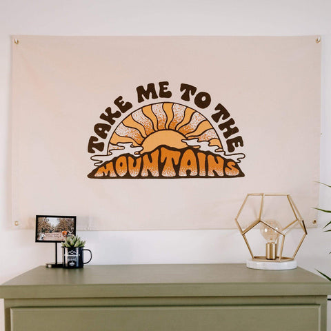 "Take Me To The Mountains" Trek Light canvas flag with sunrise graphic, hand-sewn on natural canvas, perfect for any adventure lover's space.
