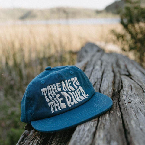 Take Me To The River Hat by Trek Light on a rustic log, perfect for Twinsie adventures with matching adult and kids sizes.