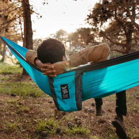Relaxing in a Trek Light hammock in a serene forest setting, perfect for outdoor adventures and peaceful naps.