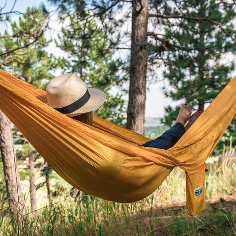 Relaxing in a Trek Light yellow banana hammock under lush trees, enjoying carefree moments in nature.