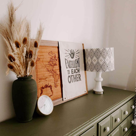"Be Excellent To Each Other" canvas flag by Trek Light on a decorated sideboard with a modern lamp and rustic decor.