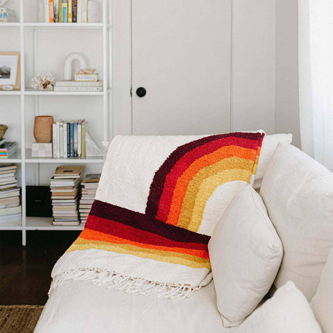 Cozy Trek Light Bowie Blanket draped on a sofa, showcasing vintage rainbow design for sustainable and stylish comfort.