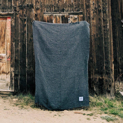 Greyson Blanket: cozy, handwoven, and beautiful, made from recycled materials. A versatile Trek Light companion against rustic wood backdrop.