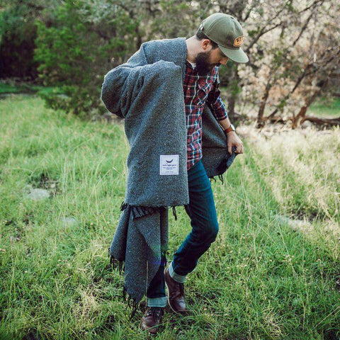 Man in nature wrapped in Greyson Blanket, cozy and beautiful, handwoven from recycled clothing materials by Trek Light.