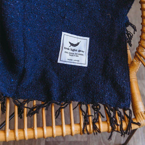 Navy Newport Blanket by Trek Light draped on a chair, perfect for outdoor festivals; embrace music and comfort with style.