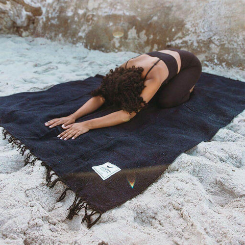 Person practicing yoga on navy Newport Blanket by Trek Light Gear, set on sandy beach.