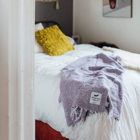 Lavender Sonoma Blanket draped on bed, handwoven from recycled materials; cozy, beautiful, and versatile home decor addition. By Trek Light.