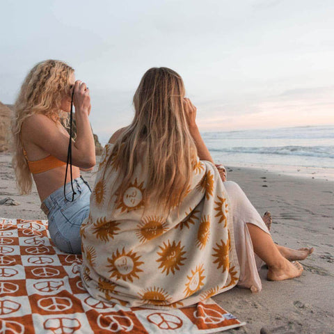 Two people on a sunny printed towel at the beach, enjoying a serene ocean view.