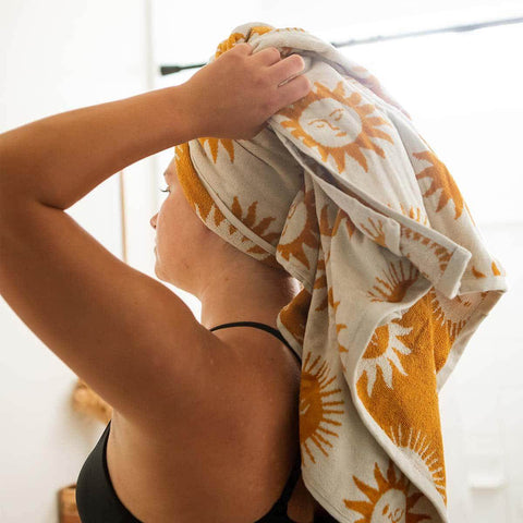 Woman wrapping hair in a sun-patterned towel, highlighting the Trek Light comfortable and stylish bath accessory for a cozy feel.