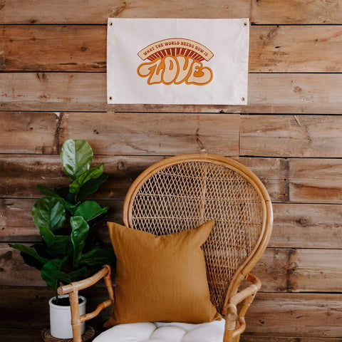 Trek Light 'What The World Needs Now' Love Canvas Flag, hand-screened on natural cotton, displayed above cozy chair and plant.