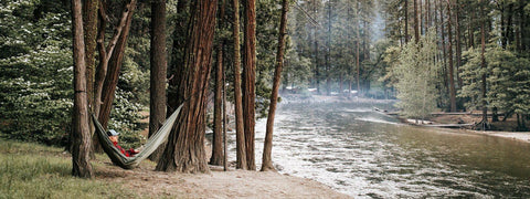 Serene river scene with Trek Light hammock strung between trees, perfect for nature relaxation.