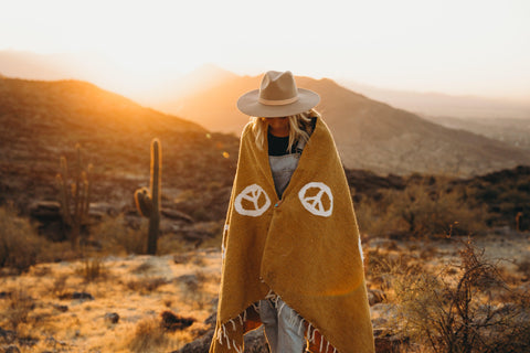 Trek Light bestselling blanket wrapped around a person in a warm sunset desert scene with cacti.