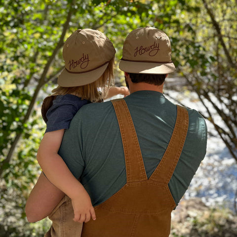 Father and child wearing matching Trek Light 'Howdy' hats, enjoying a sunny trek through the woods.