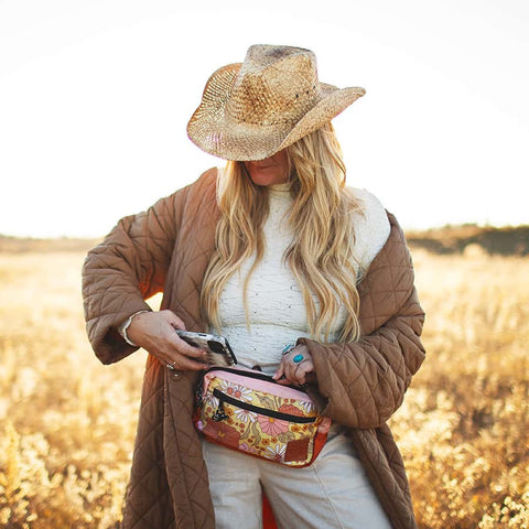 Woman wearing stylish Trek Light Everyday Fanny Pack, floral design, outdoors. Functional hip pack to shoulder sling conversion. Water resistant.