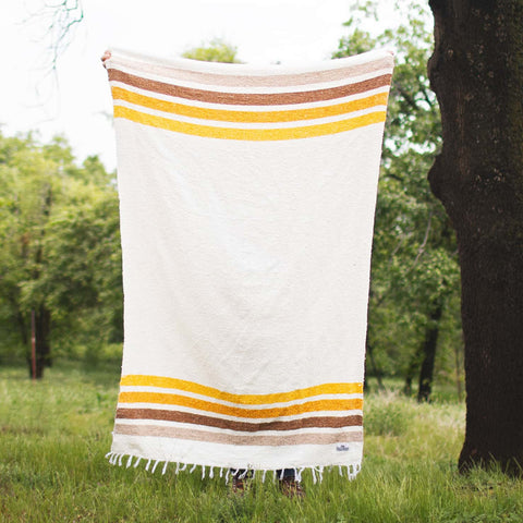 Alt Tag: Golden Age Blanket with yellow and brown stripes, handwoven from recycled materials, displayed outdoors.
