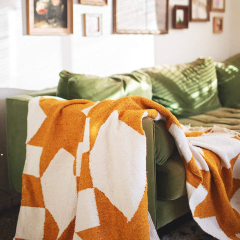 Cozy Goldie Blanket draped on sofa, showcasing handwoven geometric design, made from recycled clothing materials. Beautiful and versatile. By Trek Light.