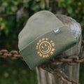 Trek Light Happy To Be Here Beanie with embroidered smiley, perfect for warmth and style outdoors.