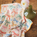 Holiday Bows Kitchen & Tea Towel showcasing colorful bows, eco-friendly and quick-drying, adorned with scissors and vase.