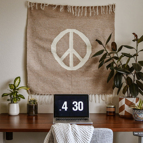 Cozy workspace with a laptop showing 4:30 PM, surrounded by plants, under a woven tapestry with a peace sign. Trek Light vibes!