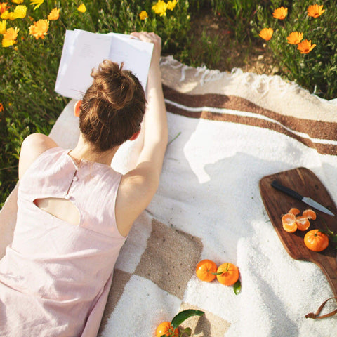 Person relaxing on a cozy handwoven North Star blanket in a meadow, highlighting its recycled materials and versatility. By Trek Light.
