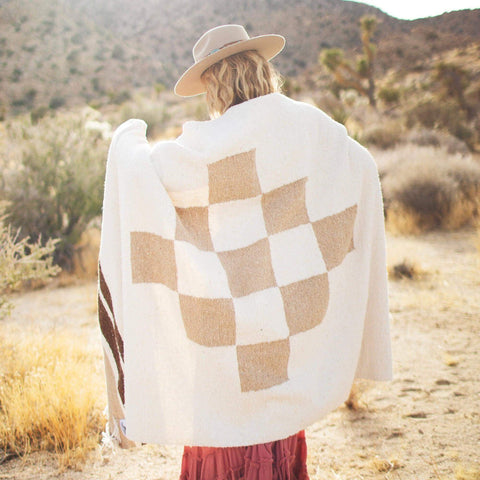Cozy person wrapped in handwoven North Star blanket made from recycled materials, displaying beautiful natural tones and checker pattern. By Trek Light.