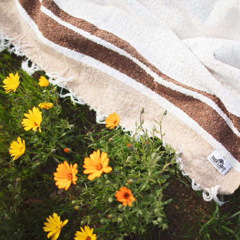 Beautiful handwoven North Star blanket made from recycled clothing materials, draped on grass with yellow flowers, cozy and versatile. By Trek Light.