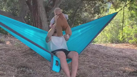 Father and child enjoying a sunny day in a durable blue Trek Light hammock, showcasing the comfort and stability of the hammock.