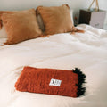 Red Rocks Blanket on a cozy bed, handwoven from recycled materials by Trek Light, showcasing its beautiful, versatile design.