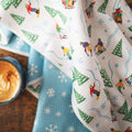 Snow Day Kitchen & Tea Towel with vibrant winter design, eco-friendly, super absorbent Grip-Tex™ fabric, displayed with a cup of coffee.