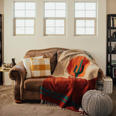 Cozy Trek Light Arizona Blanket on a couch, handwoven from recycled materials, featuring a desert sunset and cactus design. Beautiful and versatile.