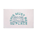 Canvas flag wall art with 'This Must Be The Place' text and tropical design, featuring Trek Light's handcrafted quality and brass grommets.