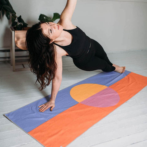 Woman practicing yoga on a vibrant Trek Light mat in a sunlit room, showcasing balance and tranquility with a colorful backdrop.