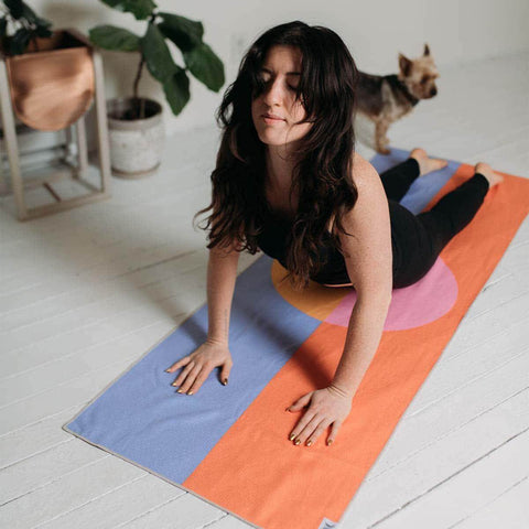 Person practicing yoga on colorful Divided Sky Yoga Towel with dog watching. Eco-friendly Trek Light, made from recycled materials.