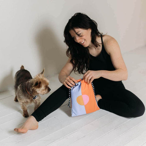 Woman sitting with a dog, holding a colorful Trek Light bag, showcasing a relaxed and joyful atmosphere.