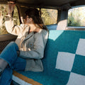 Woman in car cozy with Trek Light Dolly Blanket, embracing sustainable style with handwoven recycled material.