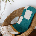 Cozy Dolly Blanket from Trek Light, handwoven with recycled materials, draped on a wicker chair, perfect for a warm, eco-friendly touch.