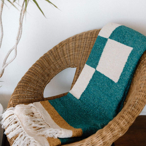 Cozy Dolly Blanket from Trek Light, handwoven with recycled materials, draped on a wicker chair, perfect for a warm, eco-friendly touch.