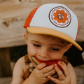 Toddler wearing Trek Light Earth Day hat, enjoying watermelon outdoors. Eco-friendly 5-panel snapback for everyday adventures.