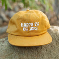 Trek Light 6-Panel Snapback Hat - Happy to Be Here embroidered message on mustard cotton twill, flat brim, unisex fit.
