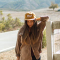 Woman wearing 'Happy To Be Here' hat by Trek Light on a peaceful countryside walk.