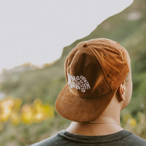 Person wearing Home Sweet Van corduroy hat with scenic backdrop, celebrating Trek Light's van life style and adventure.