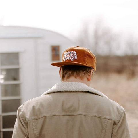 Man wearing Home Sweet Van corduroy hat in front of camper, celebrating van life with Trek Light style.