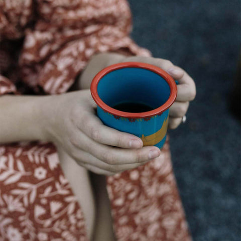 Person holding a colorful Trek Light Hug Mug enamel mug, perfect for cozy beverages by the campfire.
