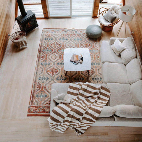 Cozy living room with a striped blanket, geometric rug, sofa, and wood-burning stove, featuring a modern, rustic decor style.