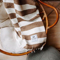 Trek Light Ocelot Blanket draped over a cozy chair, showcasing brown and white stripes, inspired by Salvador Dali's pet ocelot.